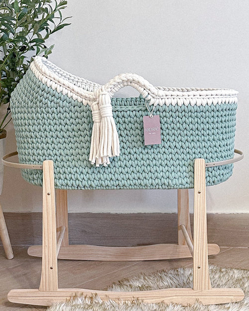 Knitted baby Moses basket on a stand with a plant in the background